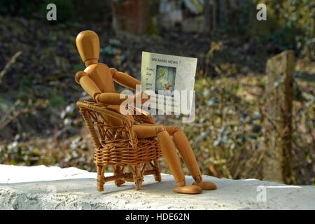 Wooden figure sitting on patio chair and reading newspaper Stock Photo