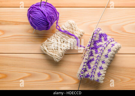 purple and white woolen yarn and knitted socks with a pattern on wooden boards Stock Photo
