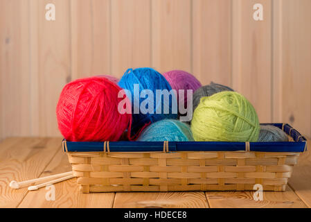straw basket packed full of woolen threads on a wooden table Stock Photo