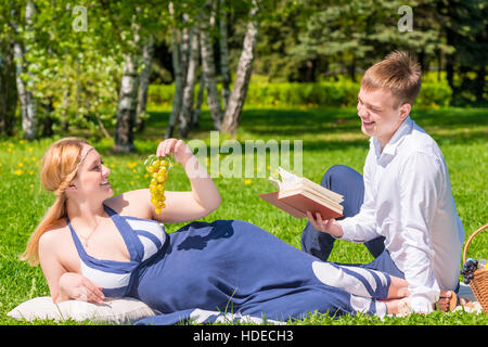 Pregnant woman with grape and her husband with a book on the picnic Stock Photo