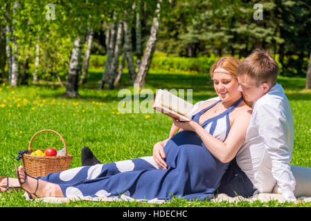 young pregnant couple in a park reading a book about pregnancy and childbirth Stock Photo