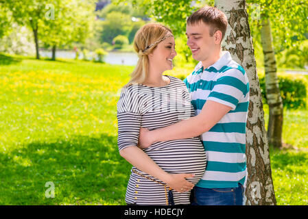 young man embracing his beautiful pregnant wife in the park Stock Photo