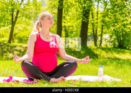 Pregnant woman meditating in a park in the lotus position Stock Photo