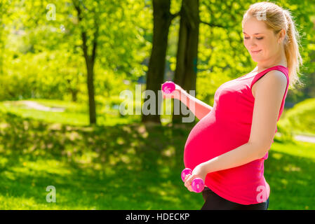 pregnant woman in a pink shirt doing exercises with dumbbells Stock Photo