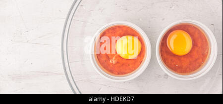 Raw eggs with tomatoes in the ramekins on the white  wooden table wide screen Stock Photo