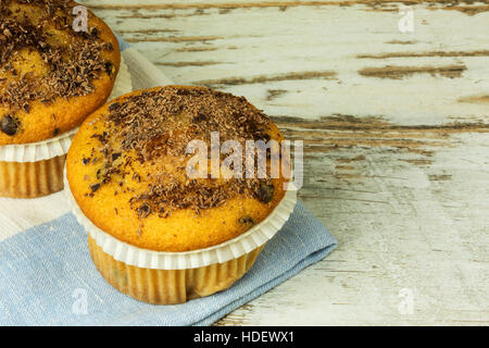 Two sponge muffins sprinkled with grated black chocolate on old wooden table. Close, flat, horizontal view. Stock Photo