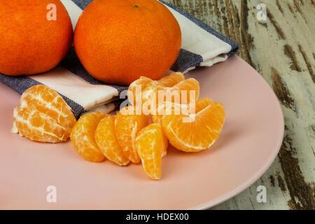 Two mandarin, tangerine, whole and one peeled the pieces on a pink plate in vintage style. Close, horizontal view from the top. Stock Photo