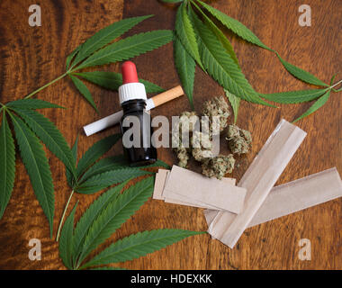 Cannabis sativa weed leafs and flower buds on wooden background with THC oil, cigarette and smoking papers Stock Photo