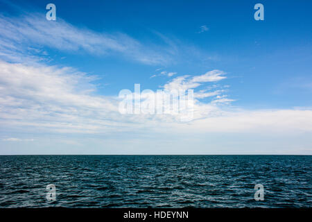 Patterned white clouds in a blue sky over a rippled azure sea. Stock Photo