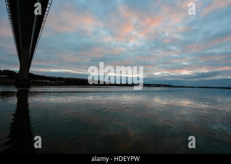 The Cleddau bridge at Pembroke Dock silhouetted against the pink and blue clouds of a November sky which are reflected in water. Stock Photo