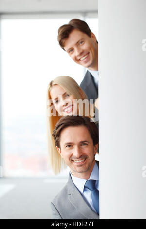 Happy business people looking out from corner in office Stock Photo