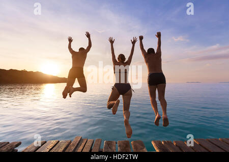 Group of happy people having fun jumping in the sea water from a pier Stock Photo