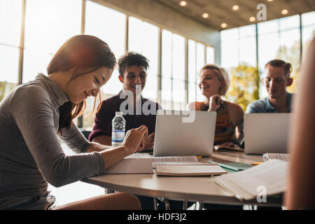 Beautiful young woman reading book with classmates studying in background. university students studying together in class. Stock Photo