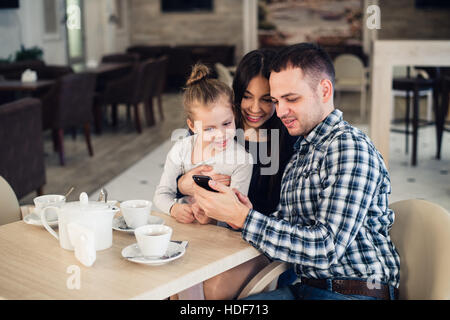 family, parenthood, technology people concept - happy mother, father and little girl having dinner taking selfie by smartphone at restaurant Stock Photo
