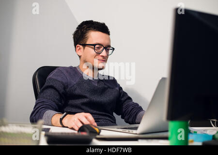 Busy working. Pensive young handsome man wearing glasses on laptop while sitting at his work place Stock Photo