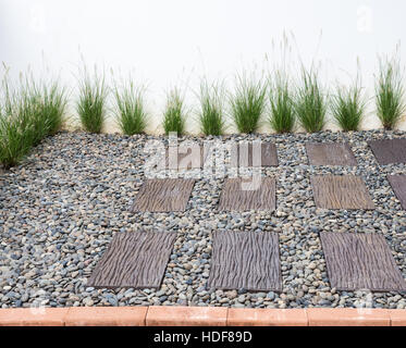 Small garden with the brick path and pebbles ground beside the white wall. Stock Photo