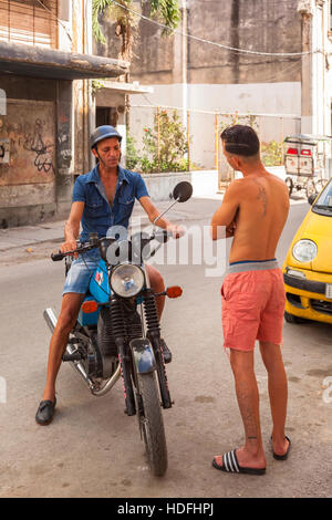 Two men (Cubans) talking on the street, one is sitting on a motorcycle in Central Havana, Cuba. Stock Photo