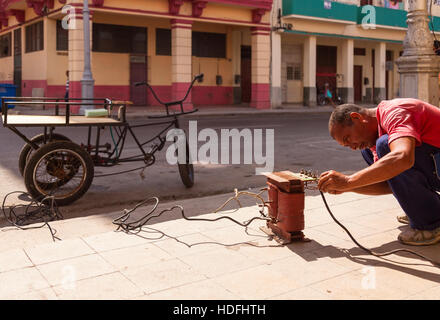 A man is working with a makeshift welder on a sidewalk in Central Havana, Cuba. Stock Photo