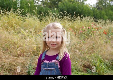 adorable school age girl standing in field on farm wearing overalls during fall autumn season Stock Photo
