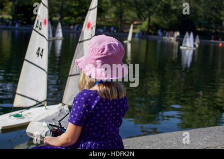 adorable young girl playing with remote control sailboats in Central Park, Manhattan, New York City Stock Photo