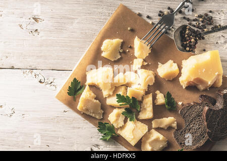 Sliced parmesan with bread , parsley and black pepper on the parchment on the white wooden table top view Stock Photo