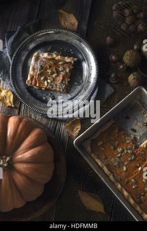 Slice of pumpkin pie on the metal plate on the wooden table with autumn gifts Stock Photo