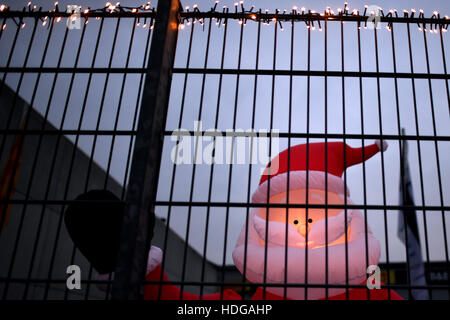 Cologne, Germany. 12th Dec, 2016. An illuminated plastic Santa Claus can be seen behind the fence in the yard of a tyre dealer in Cologne, Germany, 12 December 2016. Photo: Federico Gambarini/dpa/Alamy Live News Stock Photo