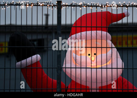 Cologne, Germany. 12th Dec, 2016. An illuminated plastic Santa Claus can be seen behind the fence in the yard of a tyre dealer in Cologne, Germany, 12 December 2016. Photo: Federico Gambarini/dpa/Alamy Live News Stock Photo