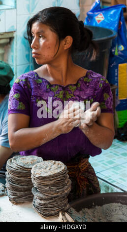 A young Mayan woman in traditional dress makes blue corn tortillas in the market at Santiago Atitlan, Guatemala. She is patting them between her hands Stock Photo