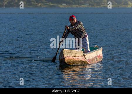 Standing Mayan man in the traditional dress of San Pedro la Laguna paddles a cayuco in early morning light on Lake Atitlan, Guatemala.   Oblique front Stock Photo