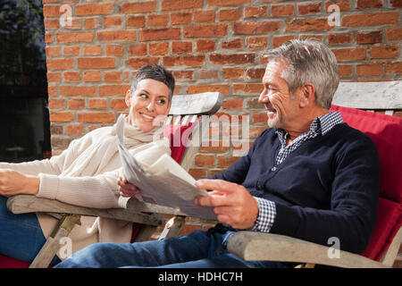 Happy woman looking at man holding newspaper while sitting in back yard Stock Photo