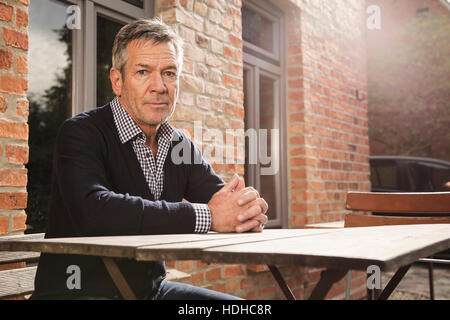 Portrait of mature man sitting at table outside house Stock Photo