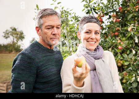 Portrait of happy woman holding apple by man in orchard Stock Photo