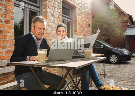 Mature man using laptop with woman holding newspaper in back yard Stock Photo
