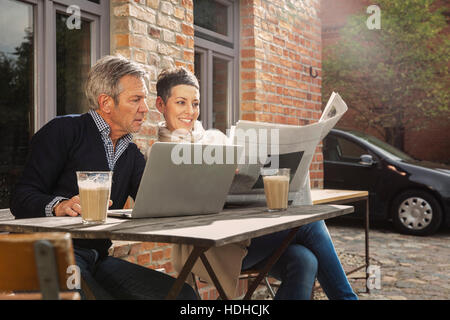 Mature man and woman reading newspaper while sitting with laptop in back yard Stock Photo
