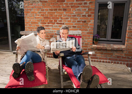 Mature couple reading newspaper while sitting in back yard Stock Photo