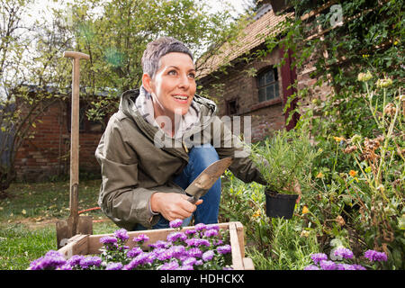 Happy woman holding trowel and pot plant in back yard Stock Photo