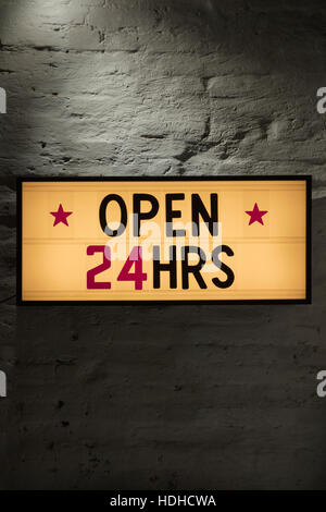 Close-up of Open 24 Hours signboard against gray wall Stock Photo