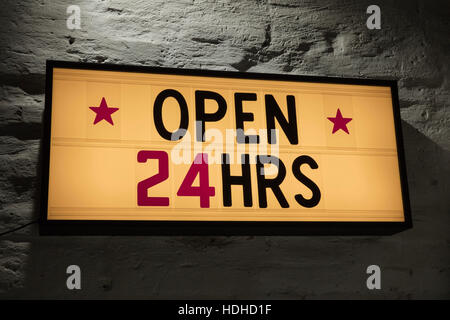 Close-up of Open 24 Hours signboard against gray wall Stock Photo