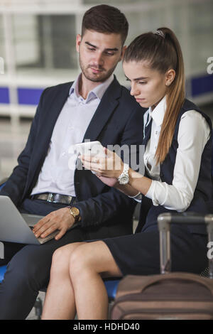 Young business couple using smart phone while waiting at airport Stock Photo