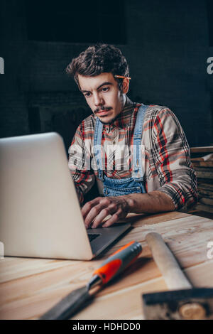 Carpenter using laptop on bench while sitting in workshop Stock Photo