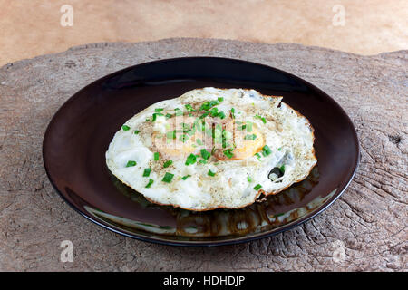 Fried eggs with double yolks sprinkle with pepper and Spring onion split in black plate on wood table. Stock Photo