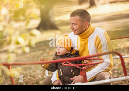 Thoughtful man sitting with baby boy on carousel at park during autumn Stock Photo