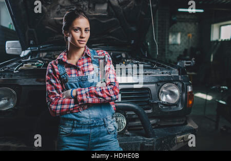 Portrait of confident female mechanic with arms crossed leaning on car at workshop Stock Photo