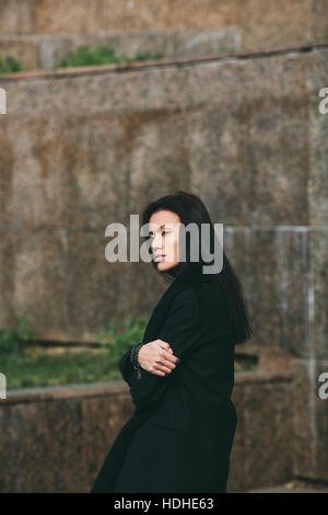 Side view of solitude woman looking away while standing arms crossed against wall Stock Photo