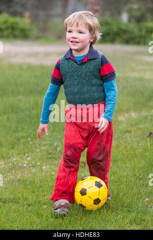 Full length of smiling boy playing soccer on field Stock Photo