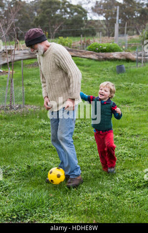 Full length of grandfather and grandson playing soccer on grassy field Stock Photo