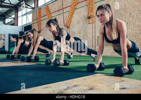 Determined female athletes doing push-ups on dumbbells at health club Stock Photo