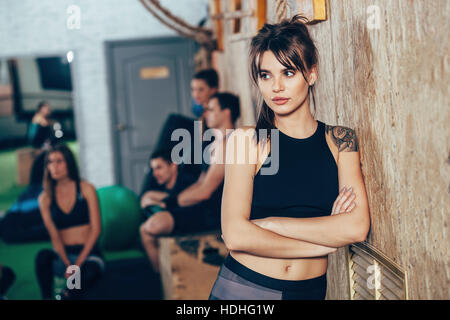 Thoughtful female athlete standing arms crossed with friends in background at health club Stock Photo