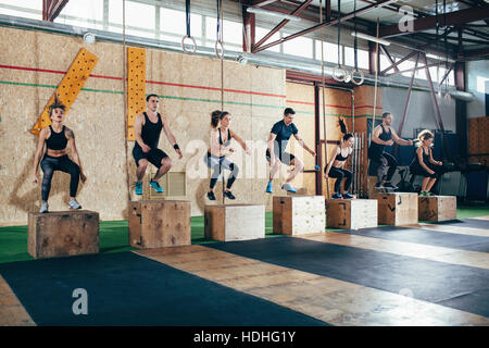 Full length of determined athletes doing box jumping at gym Stock Photo